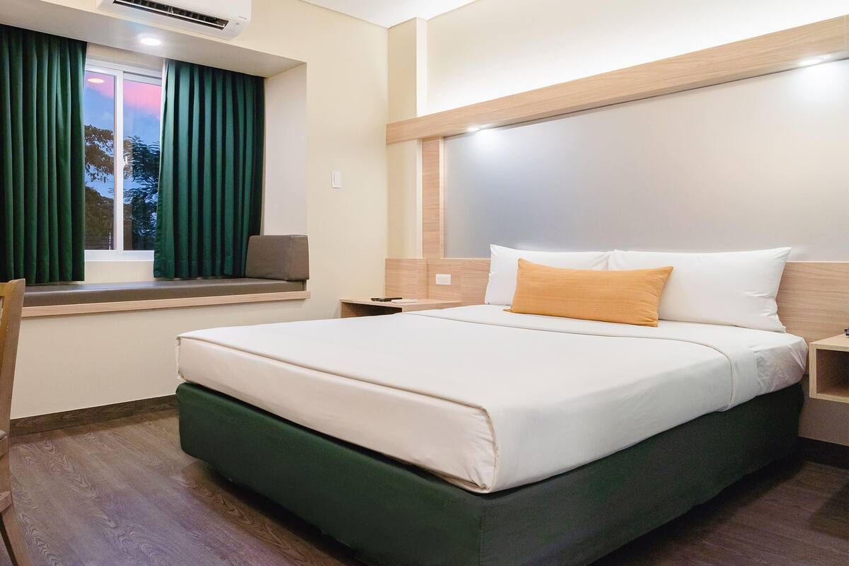 A hotel room with a large bed, a window with curtains, a bedside table, and a nightstand.