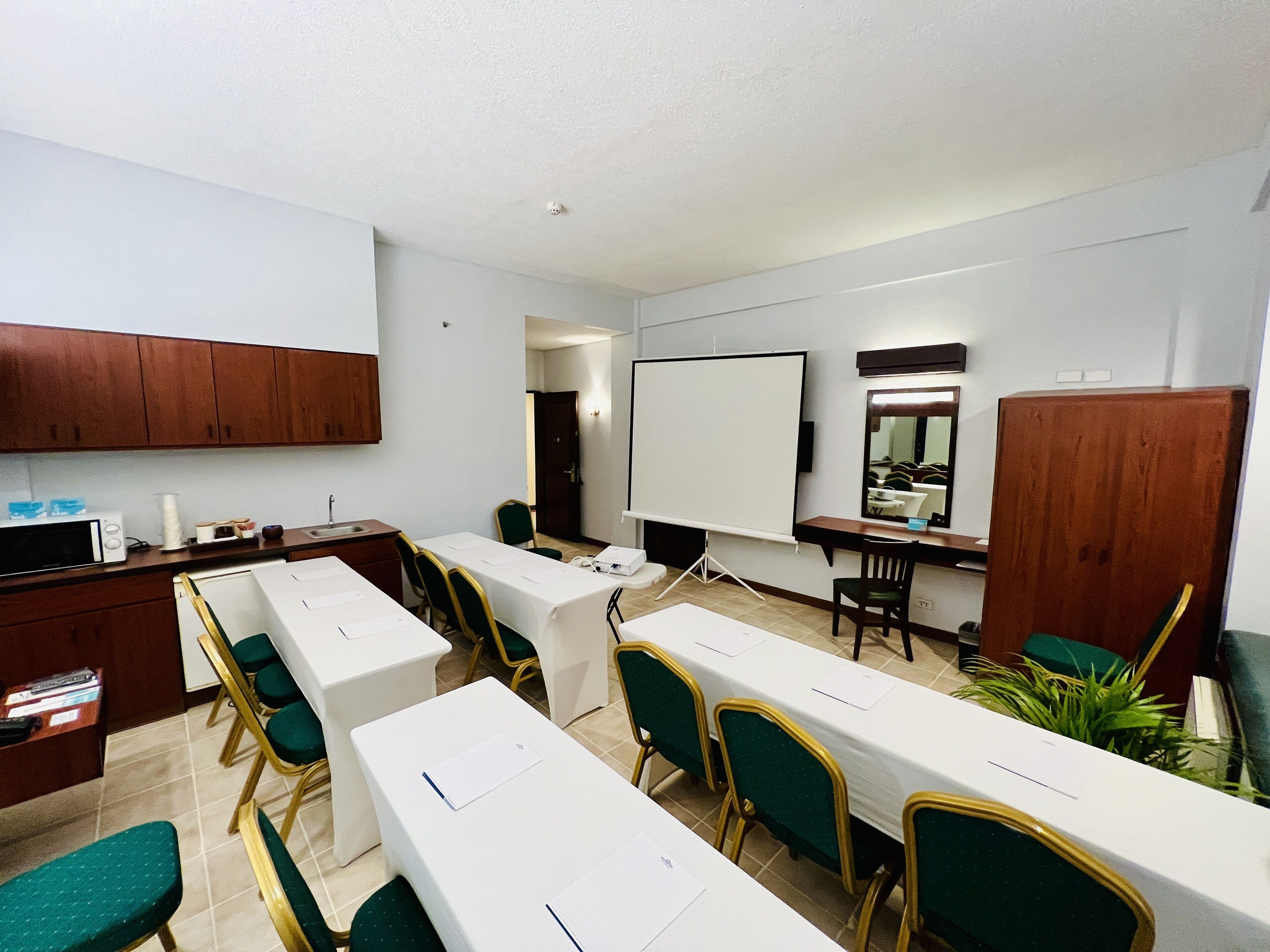 Un salón de conferencias con mesas blancas, sillas verdes, una pizarra y armarios de madera.