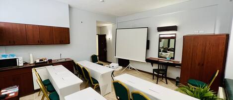 Un salón de conferencias con mesas blancas, sillas verdes, una pizarra y armarios de madera.
