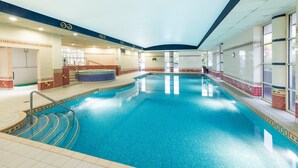 Una piscina interior amb aigua blava cristal·lina, parets de rajola i una zona de banyera d'hidromassatge al centre.