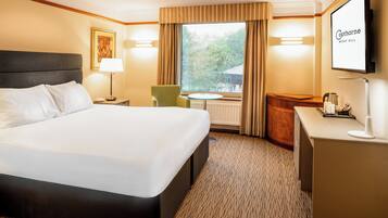Een hotelkamer met een groot bed, een bureau, een stoel, een bijzettafeltje en een aan de muur bevestigde televisie.