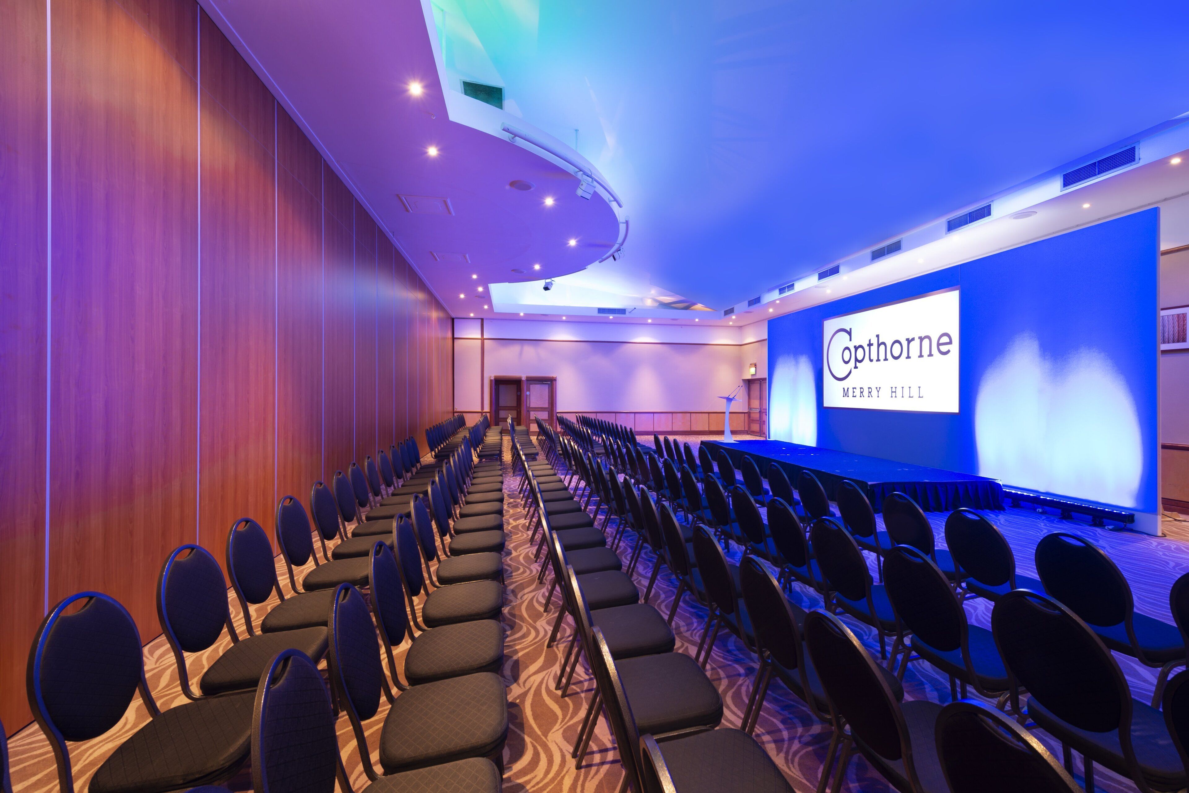 A conference room with rows of chairs facing a stage with a presentation screen.