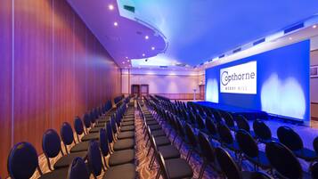 A conference room with rows of chairs facing a stage with a presentation screen.