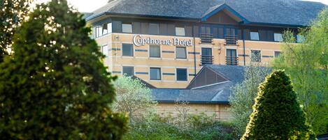 A hotel with a sign reading "Cophorne Hotel," featuring a brick facade, multiple windows, and a sloped roof.