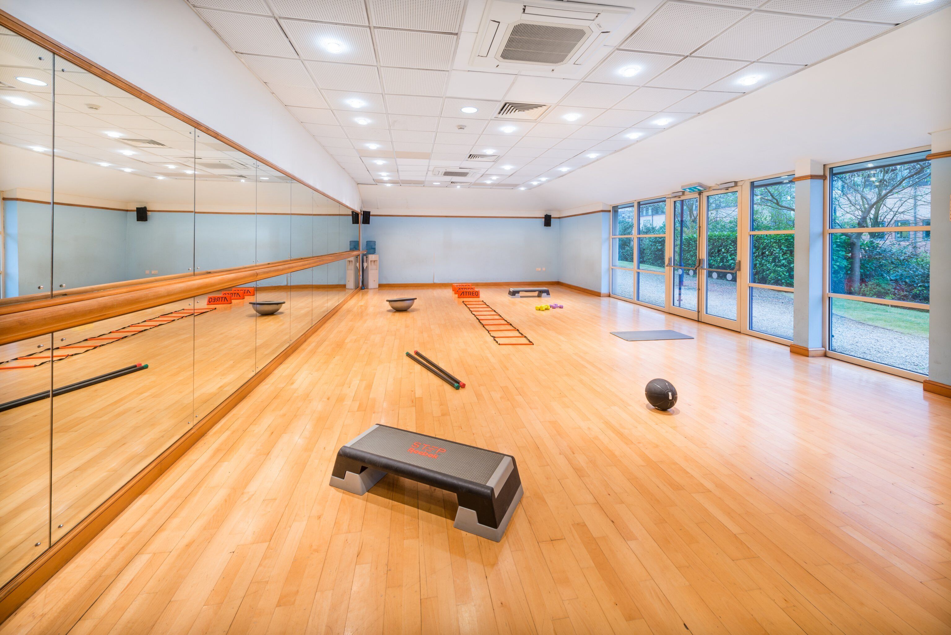 Une pièce spacieuse avec un plancher en bois, de grandes fenêtres et du matériel d’exercice.