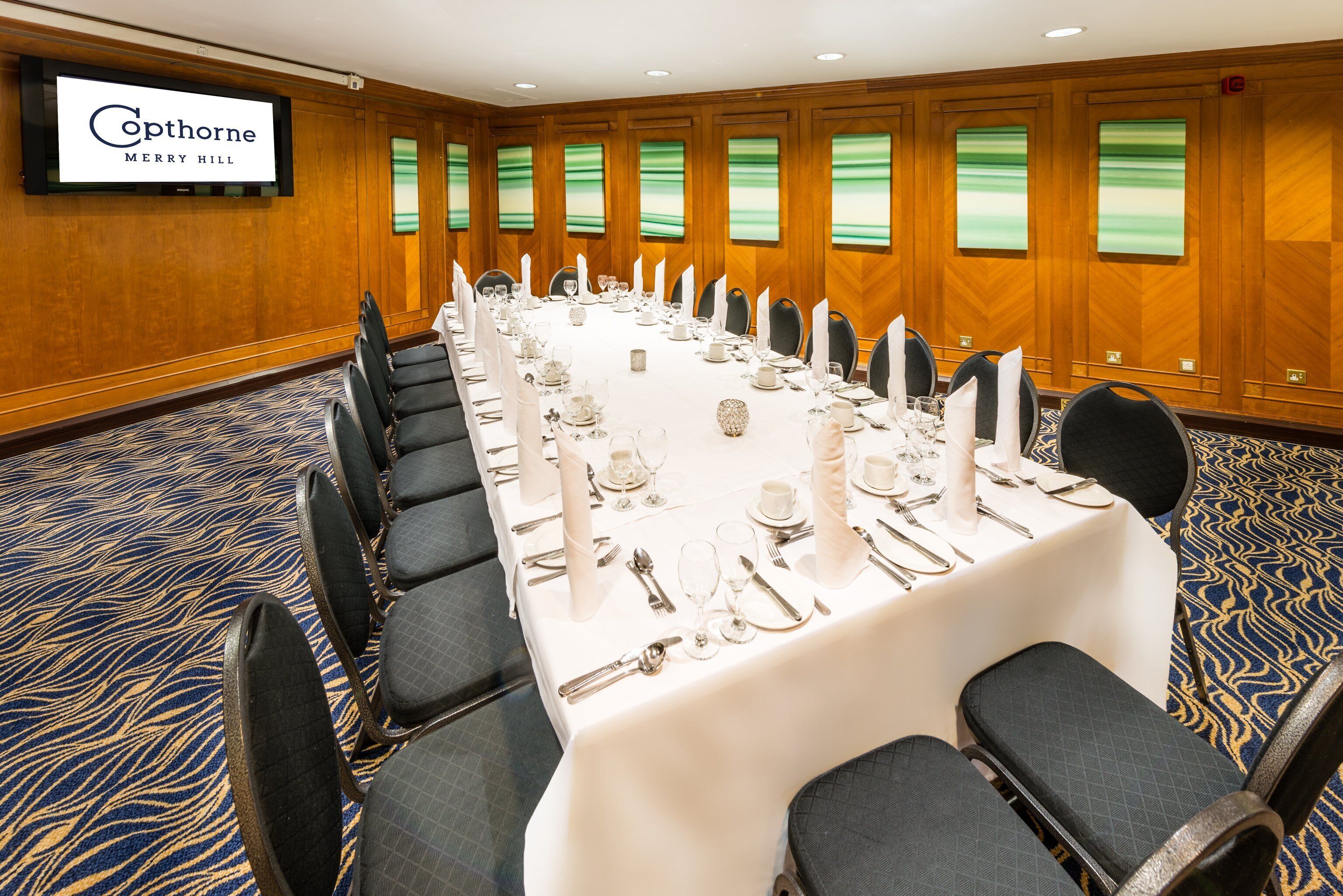 A conference room at Cophorne Merry Hill with a long table set for a meeting, surrounded by chairs, and a large screen on the wall.
