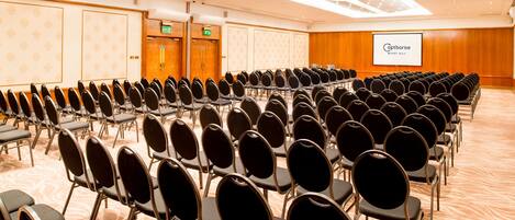 A conference room with rows of chairs, a projection screen, and a wooden wall with a patterned design.