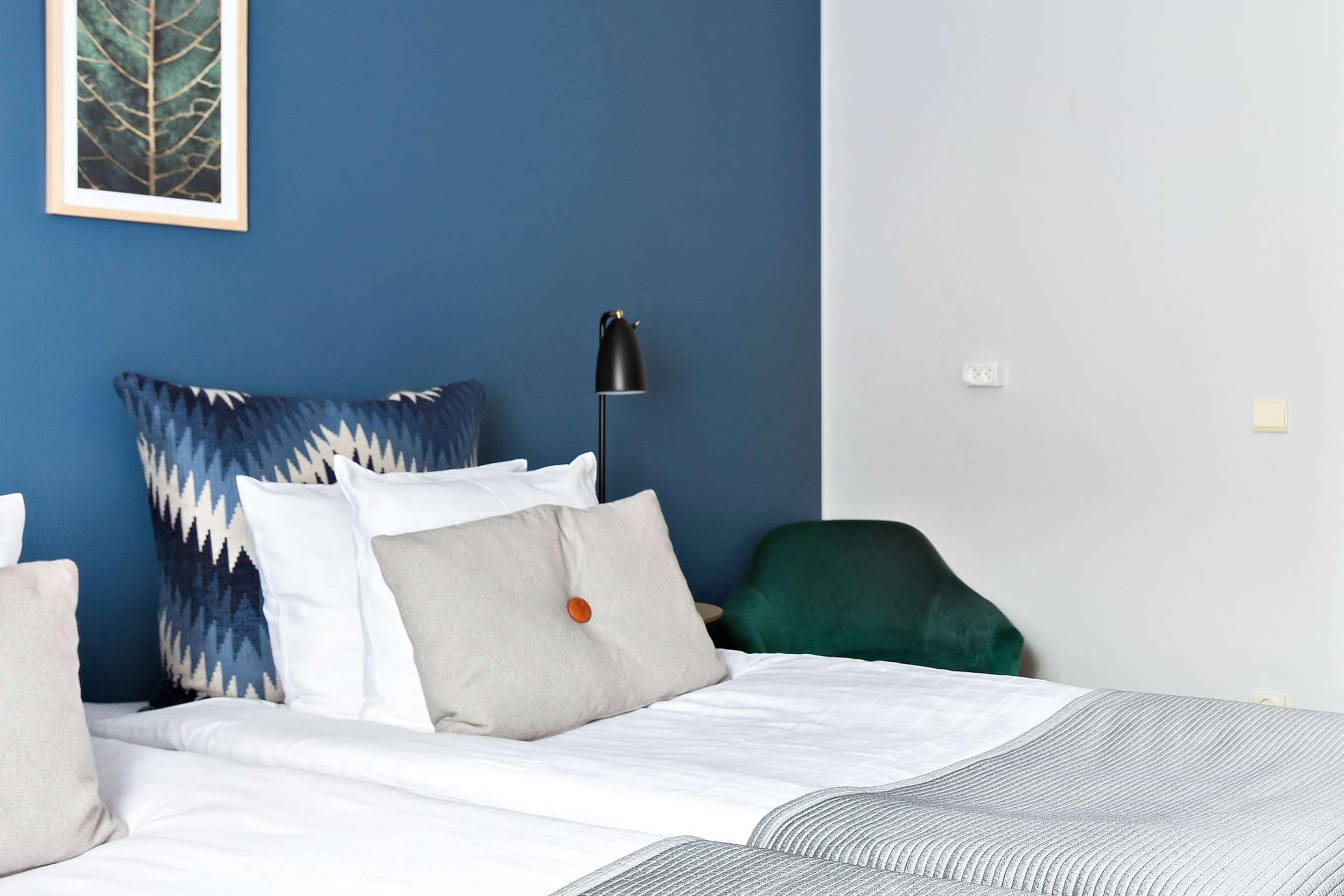 A bedroom with a bed, pillows, a desk lamp, and a chair.