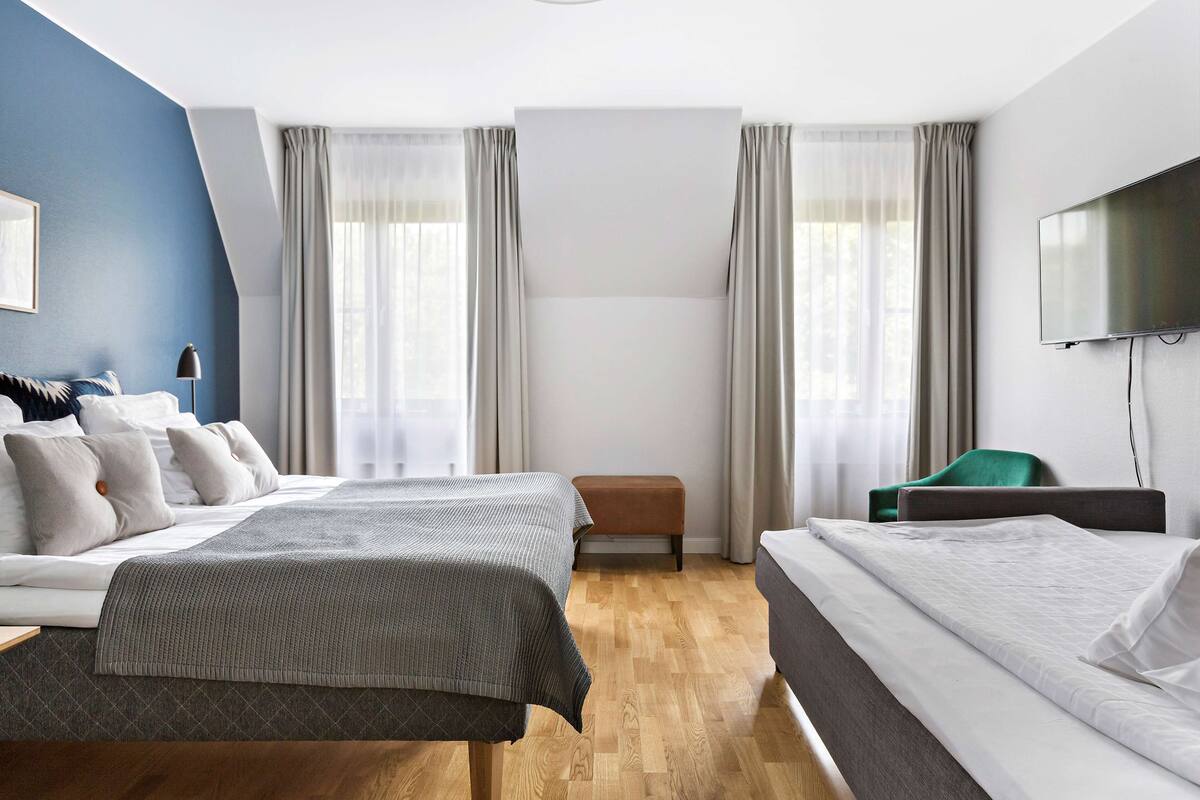 Una habitación de hotel moderna con dos camas, un televisor de pantalla plana, un escritorio y una ventana con cortinas.