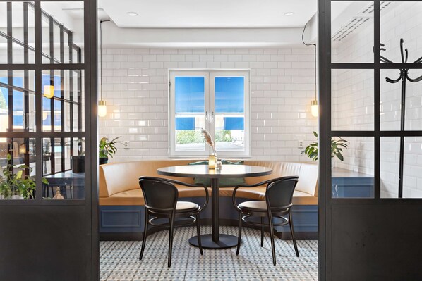 A dining area with a round table, two chairs, a bench, and a window with blinds. - Best Western Hotel Park Astoria (Enkoping)