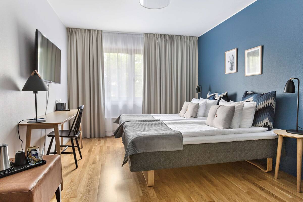 Una habitación de hotel moderna con una cama grande, un escritorio con computadora, un televisor y una cafetera.