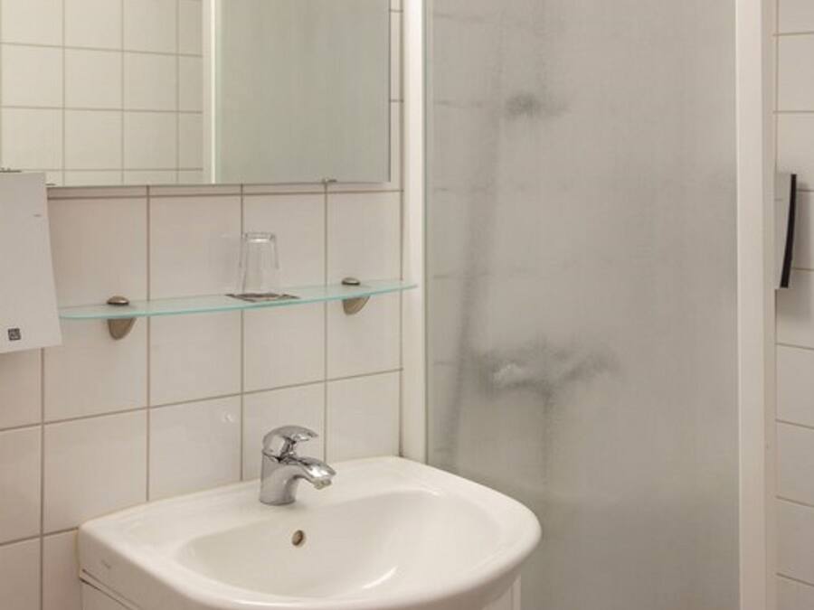 A bathroom with a white sink, a glass shelf, and a mirror.