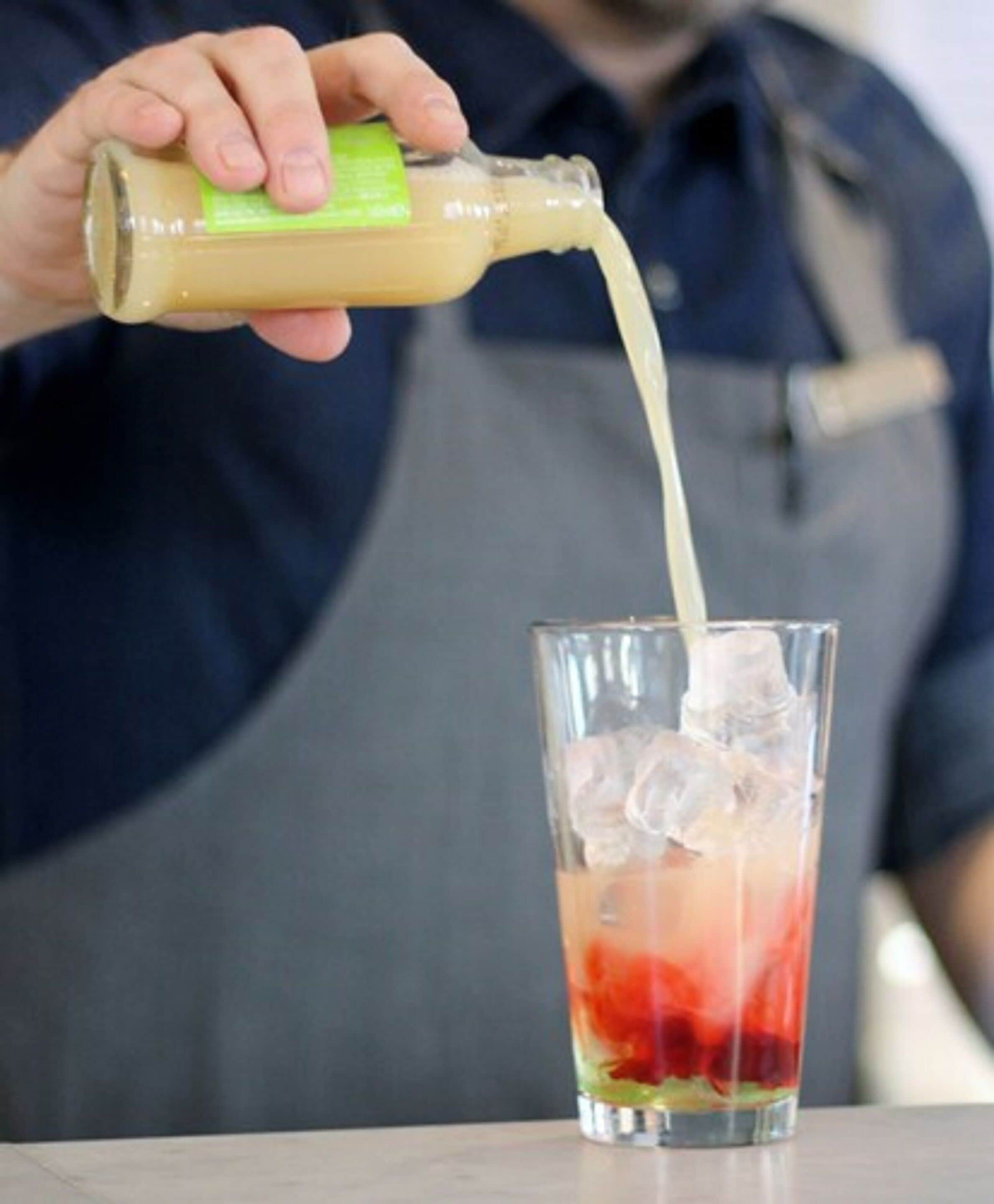 A person pouring a drink into a tall glass with ice.