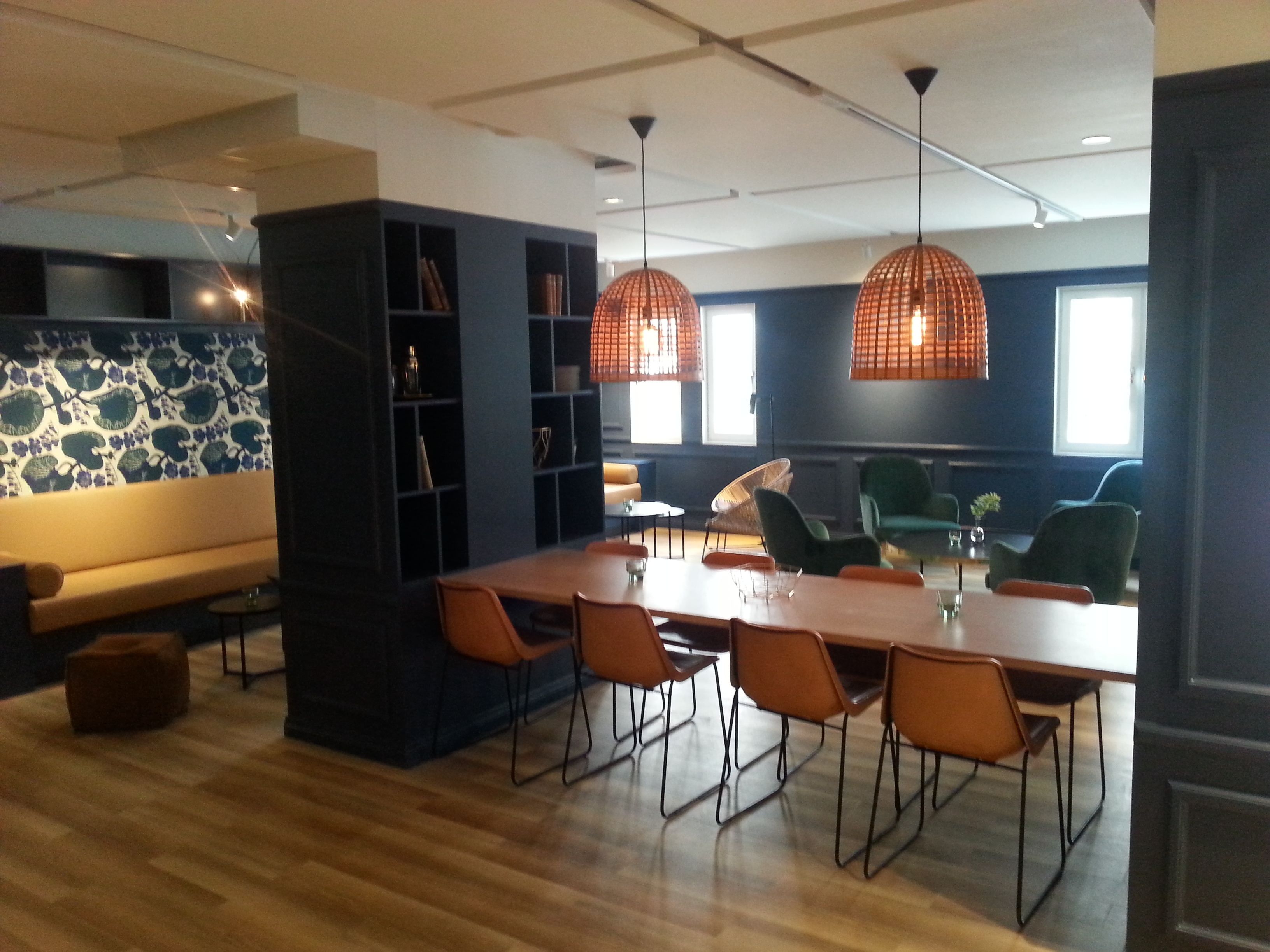 A modern dining area with a long wooden table, orange chairs, and pendant lights.