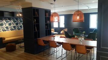 A modern dining area with a long wooden table, orange chairs, and pendant lights.