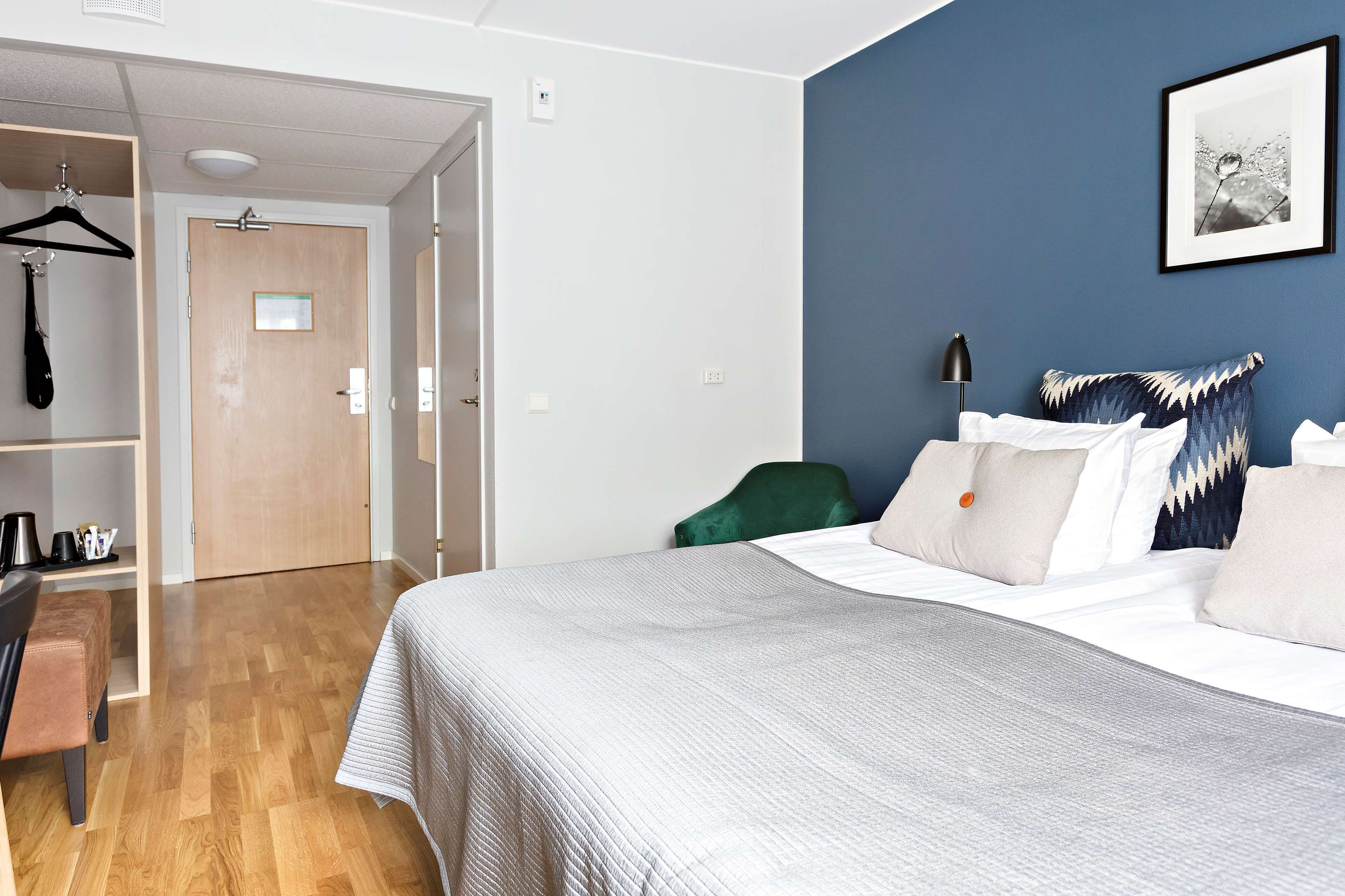 A hotel room with a bed, a desk, a chair, a wardrobe, and a door.
