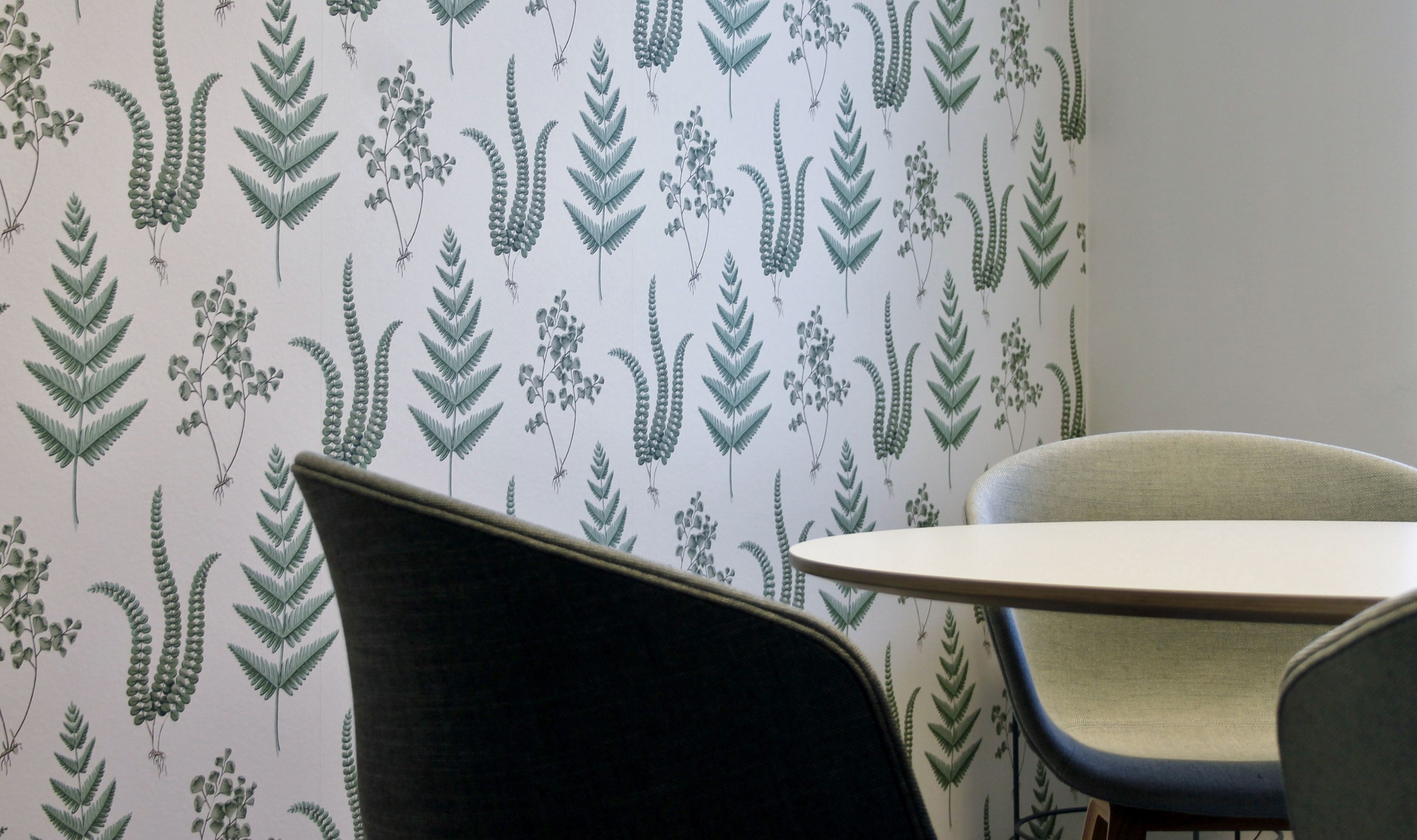 Una stanza con carta da parati a motivi decorati con disegni botanici, un tavolo rotondo e sedie moderne.