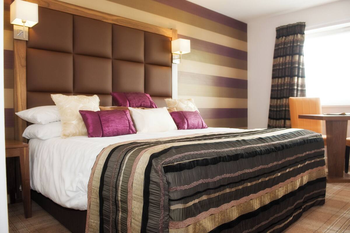 Een hotelkamer met een groot bed, hoofdeinde, bedlampen en uitzicht op het groen.