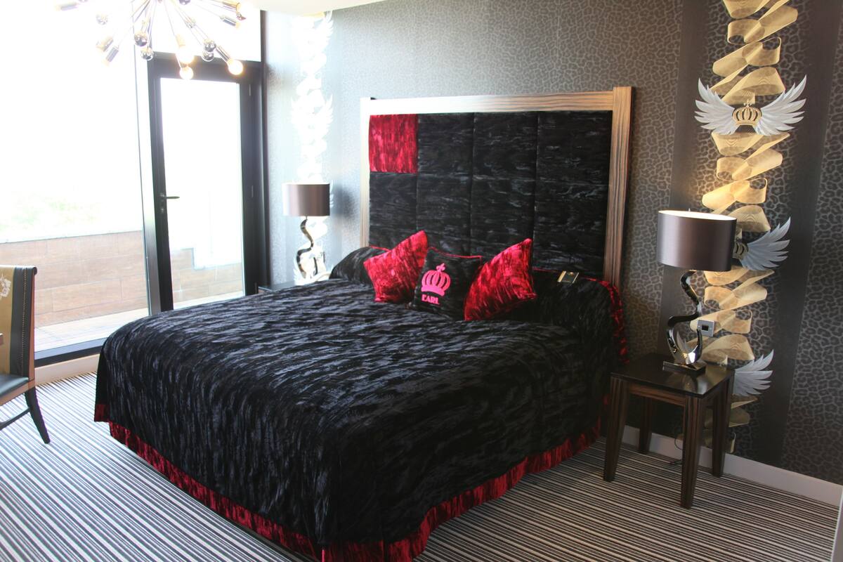 Een slaapkamer met een groot bed, een nachtkastje, een lamp en een decoratief wandobject.