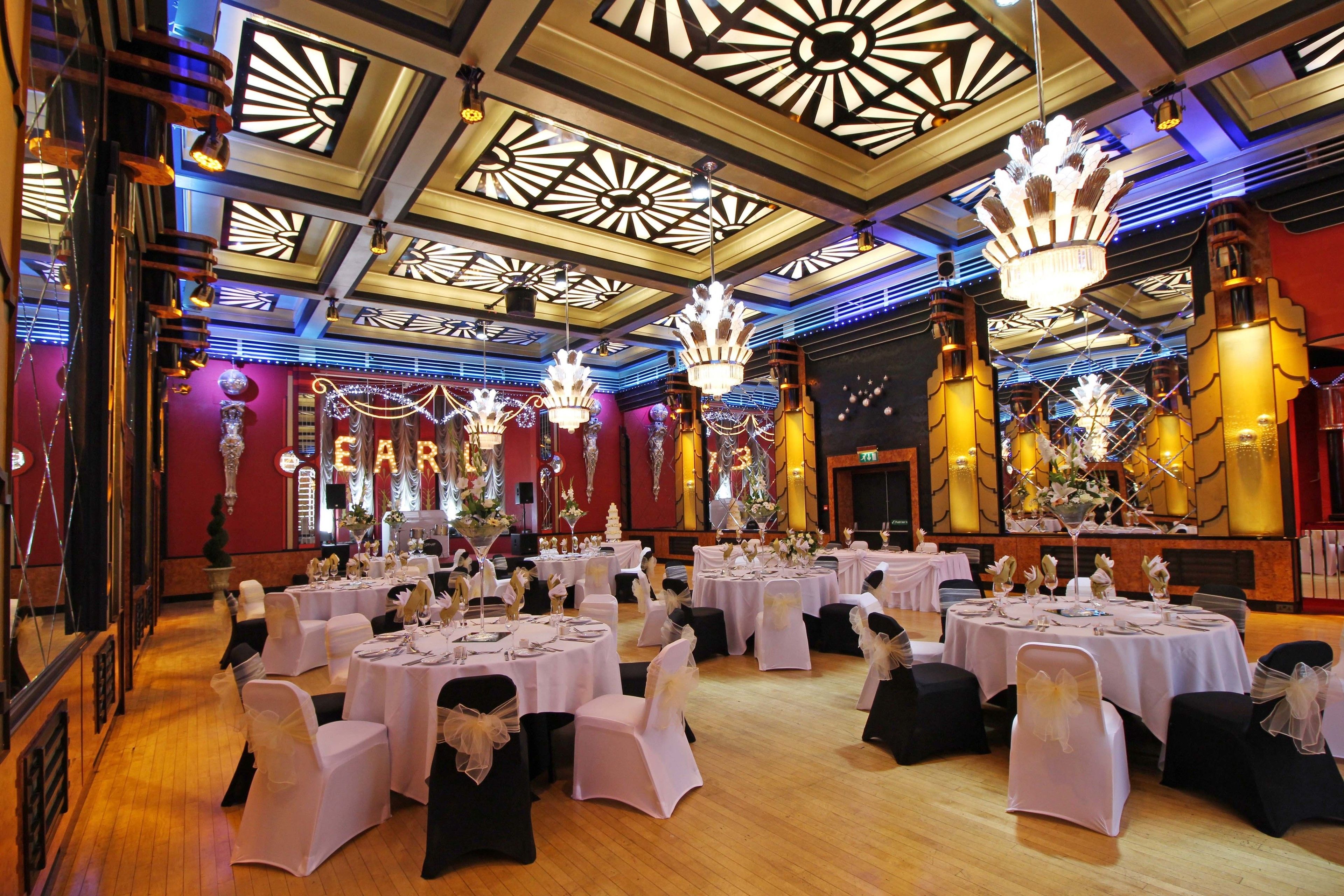 A banquet hall with round tables set for a formal event, featuring chandeliers and ornate ceiling designs.