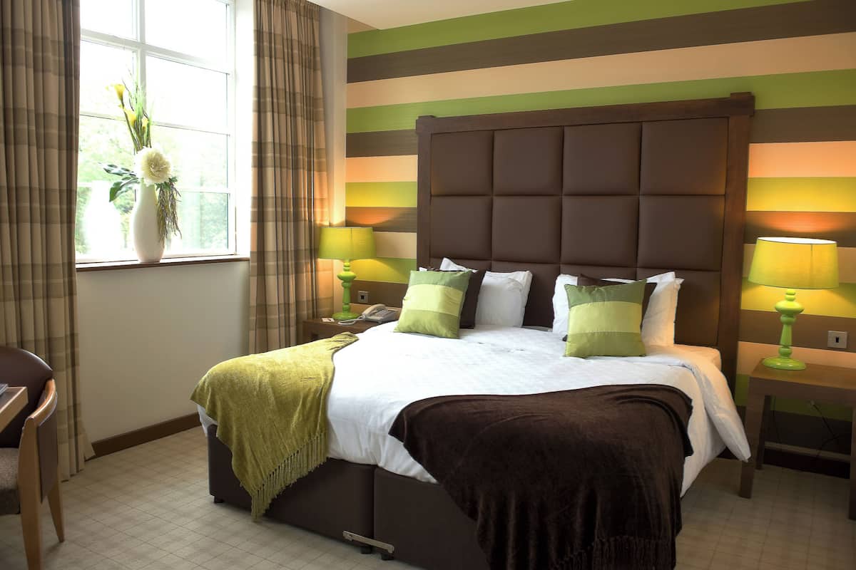 Een hotelkamer met een groot bed, twee nachtkastjes, een stoel en een raam met gordijnen.