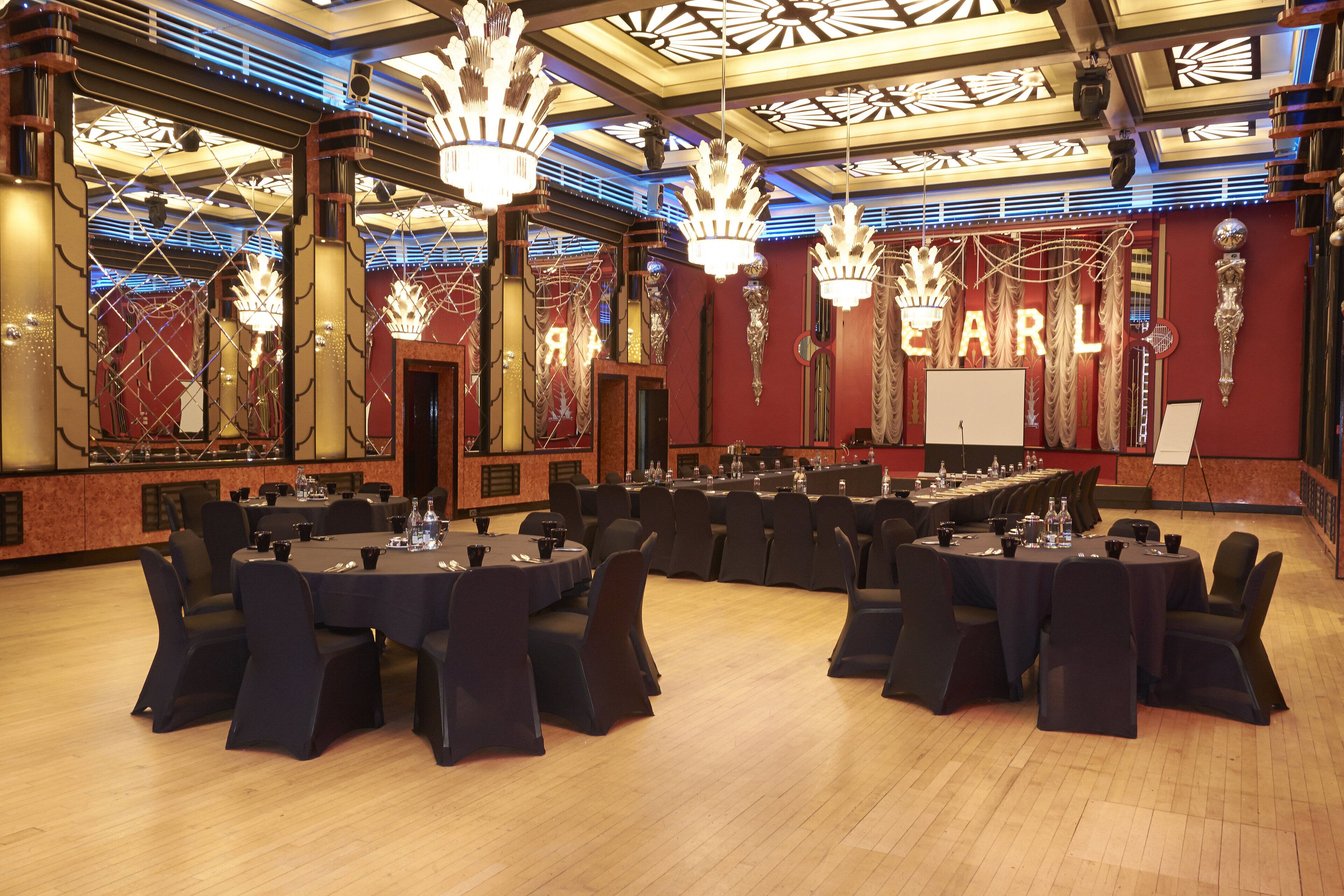 Un salón de conferencias con mesas redondas, sillas negras y candelabros.