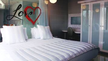 A modern bedroom with a large bed, a glass wall with a heart design, and a wardrobe.