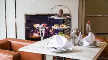 A dining table set with a three-tiered dessert stand, wine glasses, and a television in the background.