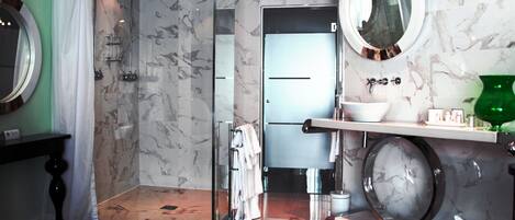 A modern bathroom with a glass-enclosed shower, a white sink with a marble countertop, and a round mirror.