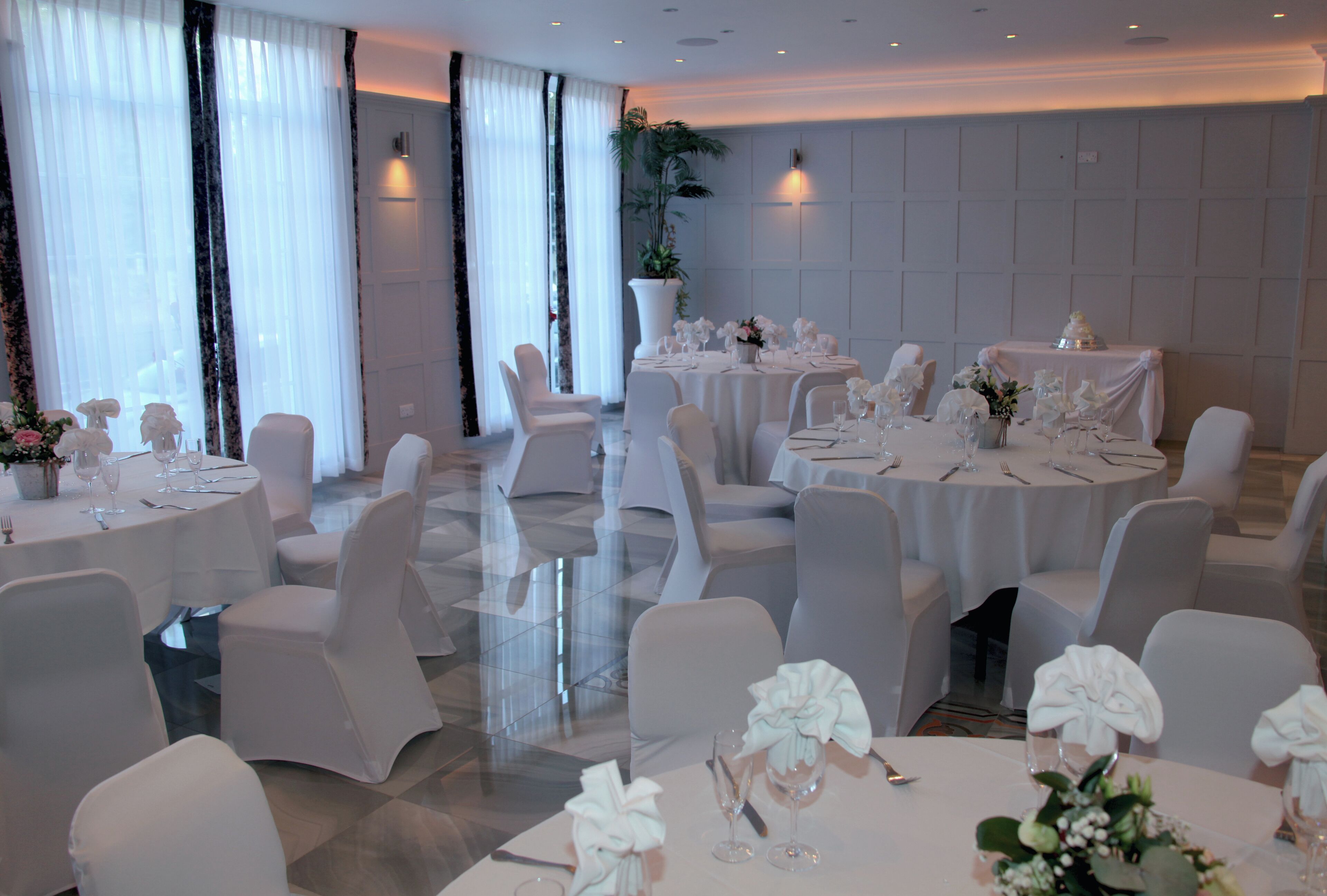 A banquet hall with round tables, white chairs, and floral centerpieces.