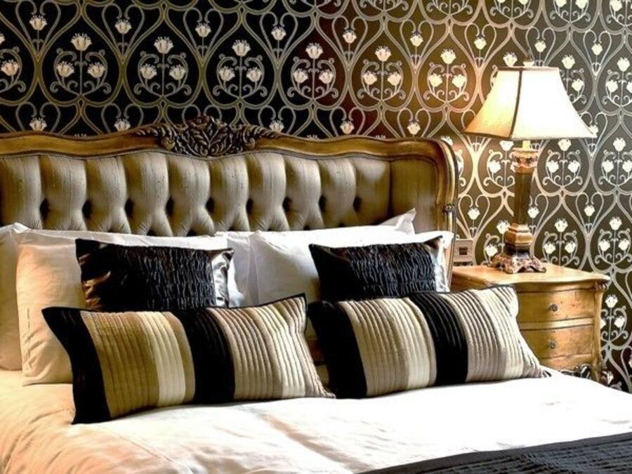 Una cama con cabecera capitonada, dos mesitas de noche con lámparas y un papel tapiz estampado.