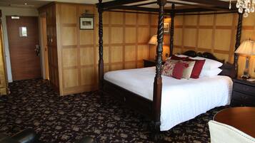 A four-poster bed with a wooden frame and white bedding, a wooden wardrobe, a desk with a lamp, and a patterned carpet.