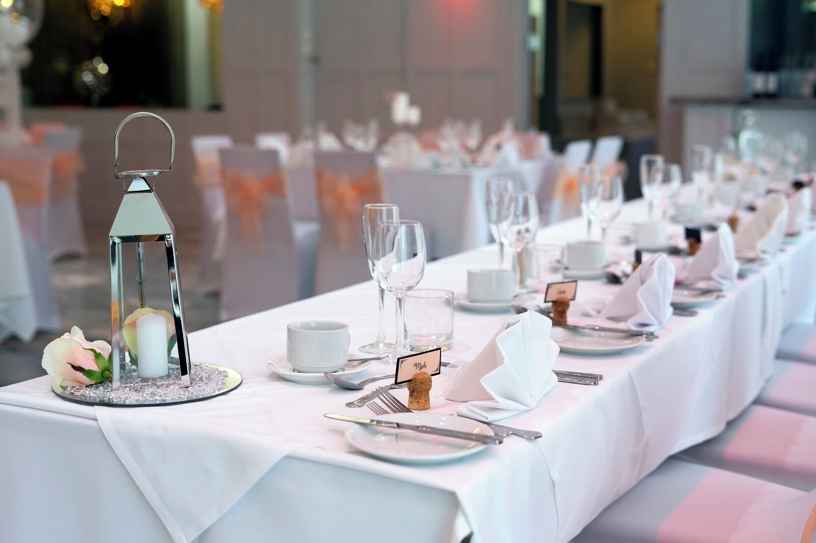 A long table set for a formal event with white tablecloths, clear glassware, and elegant napkin holders.