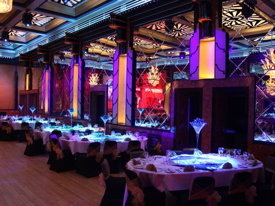 A banquet hall with round tables set for a formal event, featuring a modern chandelier and geometric ceiling design.