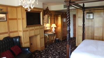 Habitación de hotel con cama con dosel, sofá de cuero, candelabro, televisor y pared de paneles de madera.