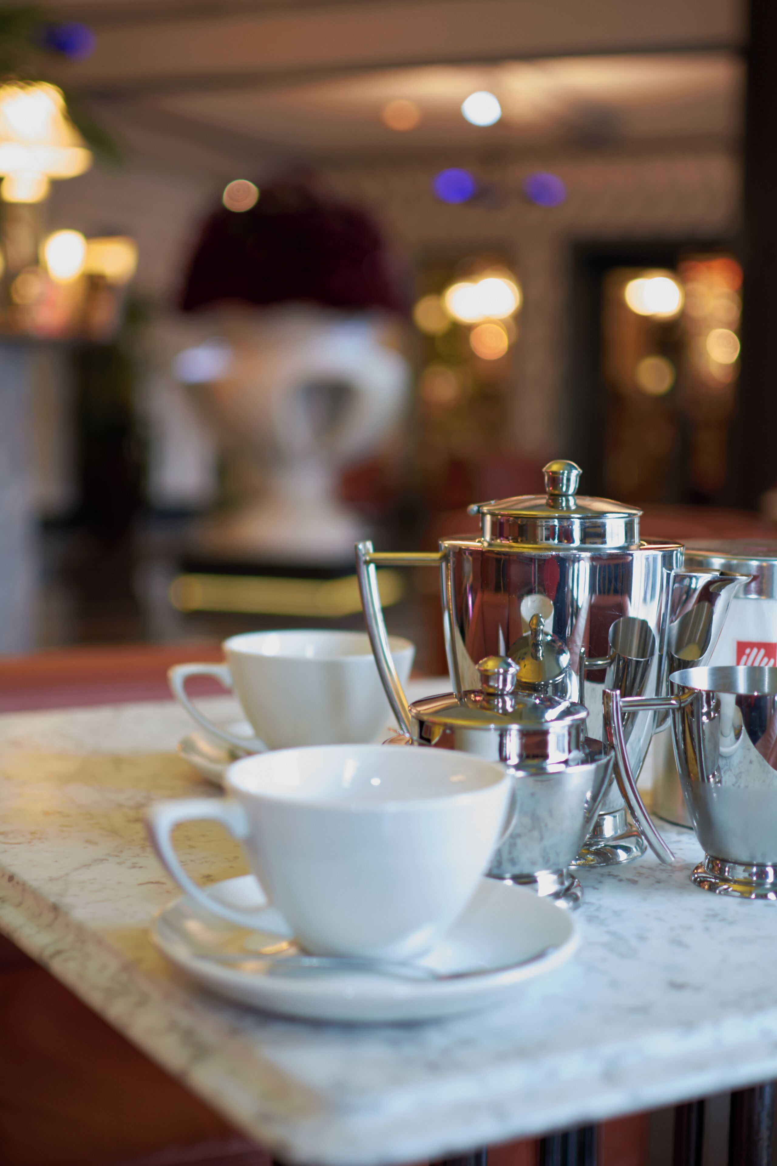 Una disposición para café con una cafetera, tazas y cucharas sobre una mesa de mármol.