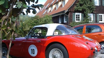 Une voiture de sport rouge d’époque, avec un toit blanc, est garée devant un bâtiment doté d’un toit en pente et de nombreuses fenêtres.