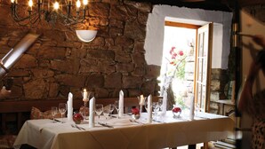 A dining table set with candles, glasses, and cutlery in a rustic stone-walled room with a chandelier.