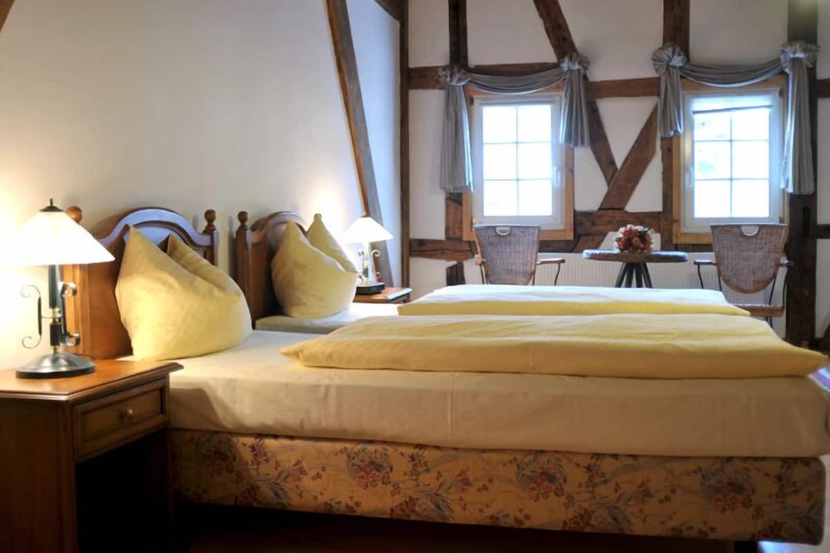 A traditional room with a bed, two chairs, a table, and a lamp.