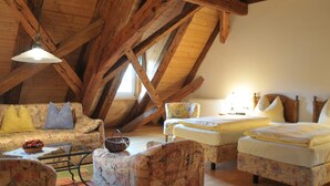 A cozy attic room with wooden beams, a sofa, two beds, and a table with a basket of flowers. - Gutshof Hotel Waldknechtshof (Baiersbronn)