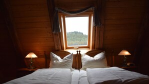 A wooden room with a bed, two bedside lamps, and a window with curtains.
