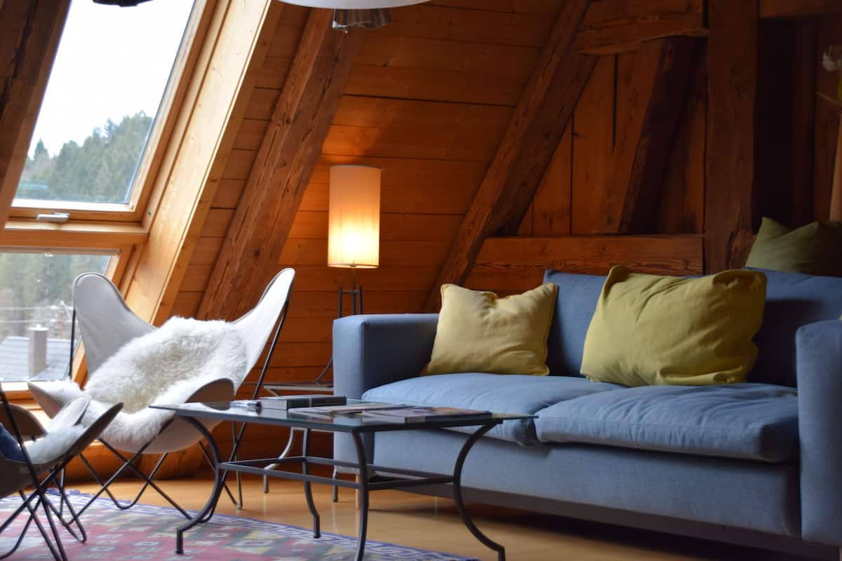 A cozy loft bedroom with a sloped ceiling, a blue sofa, a white chair, and a lamp.