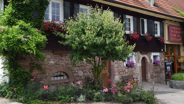 A stone building with a traditional European architectural style, featuring a wooden door, arched windows, and a bench outside.