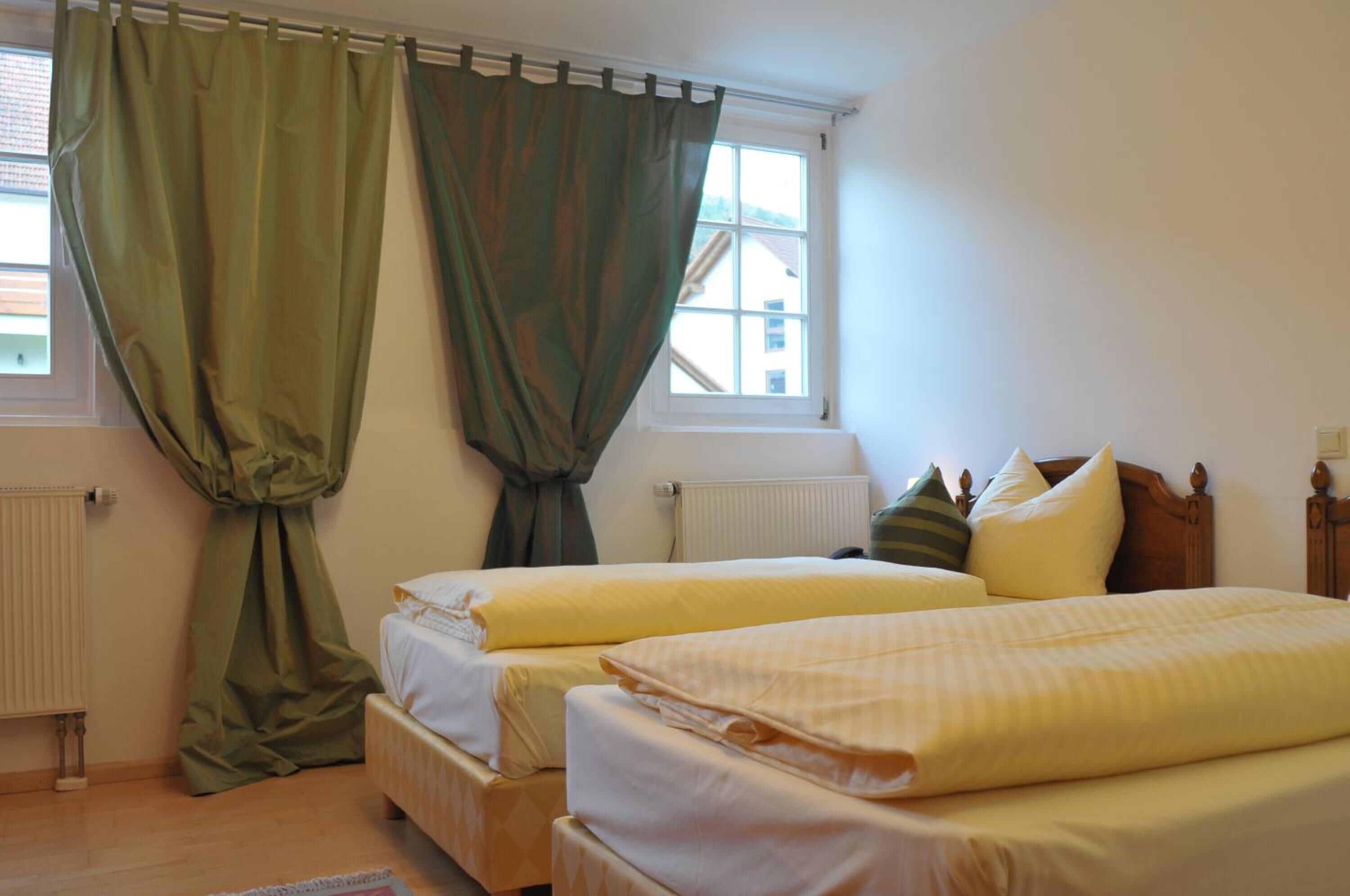 Ein Schlafzimmer mit zwei Betten, einem Fenster mit Vorhängen, einem Heizkörper und einem Holzkopfteil.