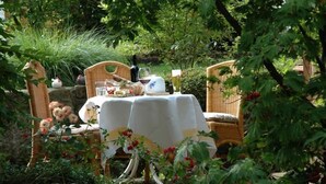 A garden setting with wicker chairs and a table set for a meal, surrounded by greenery and flowers. - Gutshof Hotel Waldknechtshof (Baiersbronn)