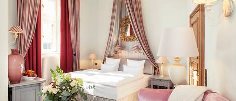 Une chambre d’hôtel avec un grand lit, des tables de chevet, une commode, un miroir et des rideaux.