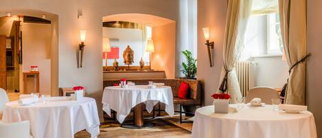 Un comedor con mesas redondas, manteles blancos y apliques de pared con velas.