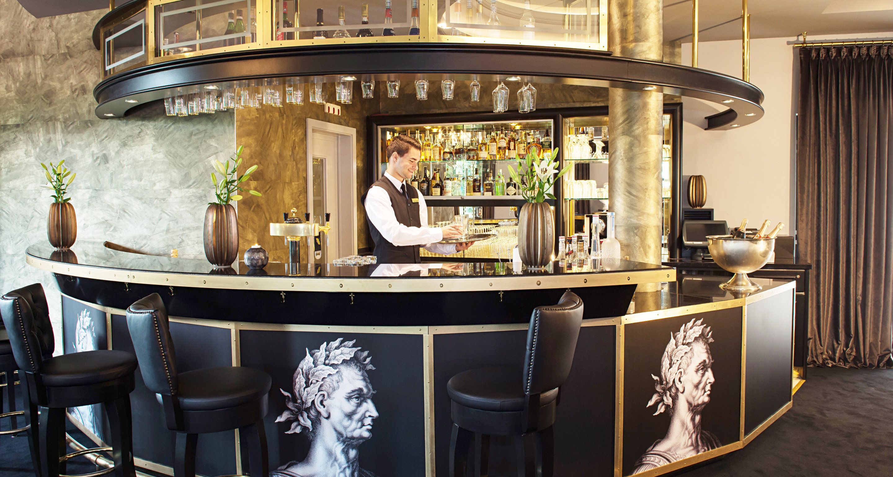 A bar area with a bartender, bar stools, and a wine display.