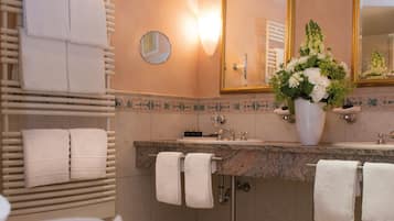 Un baño con encimera de granito, toallas blancas, un espejo redondo y un jarrón con flores.