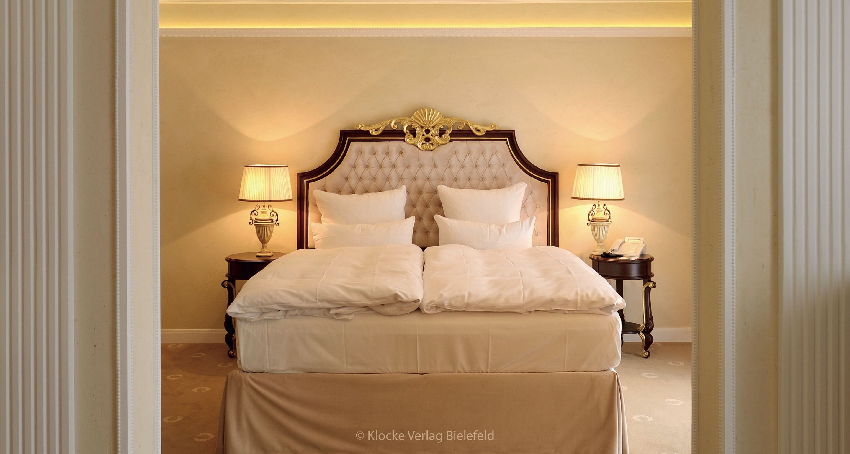 A bedroom with a large bed, two bedside tables with lamps, and a decorative headboard.